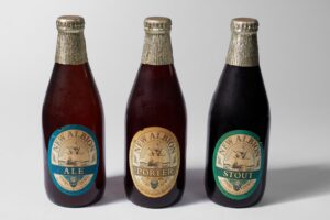 Três garrafas de cerveja, com os rótulos "ale", "porter" e "stout"