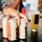 mão masculina segura em Latas de cerveja Oso x Verdant 5PM NEPA 44 cl Copo em cima de um balcão