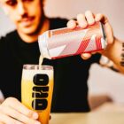 rapaz serve uma lata de OSO Brew Co Dominion x Messorem Double IPA 8,4% ABV 44 cl para um copo quase cheio. cerveja amarelo escuro.