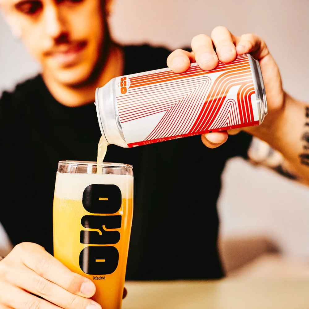rapaz serve uma lata de OSO Brew Co Dominion x Messorem Double IPA 8,4% ABV 44 cl para um copo quase cheio. cerveja amarelo escuro.